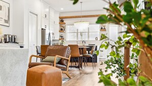 A modern kitchen with white cabinetry, a dining area with leather chairs, and a wooden floor. - Luxury Spa Retreat | Sauna, Hot Tub & Fire Pit (Nashville)