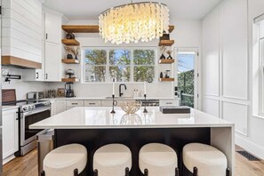 Une cuisine moderne dotée d’un grand îlot central, de meubles blancs et d’un lustre décoratif.