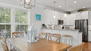 A modern kitchen with white cabinets, stainless steel appliances, and a wooden dining table with chairs.