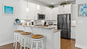 A modern kitchen with white cabinetry, a stainless steel refrigerator, a microwave, and a bar area with stools.