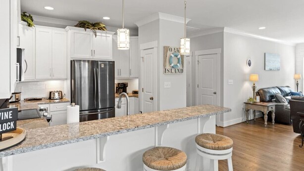 A modern kitchen with white cabinets, a stainless steel refrigerator, granite countertops, and a bar area with stools.