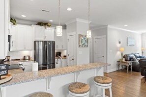 Eine moderne Küche mit weißen Schränken, einem Edelstahlkühlschrank, Granit Arbeitsplatten und einer Bar mit Hockern.