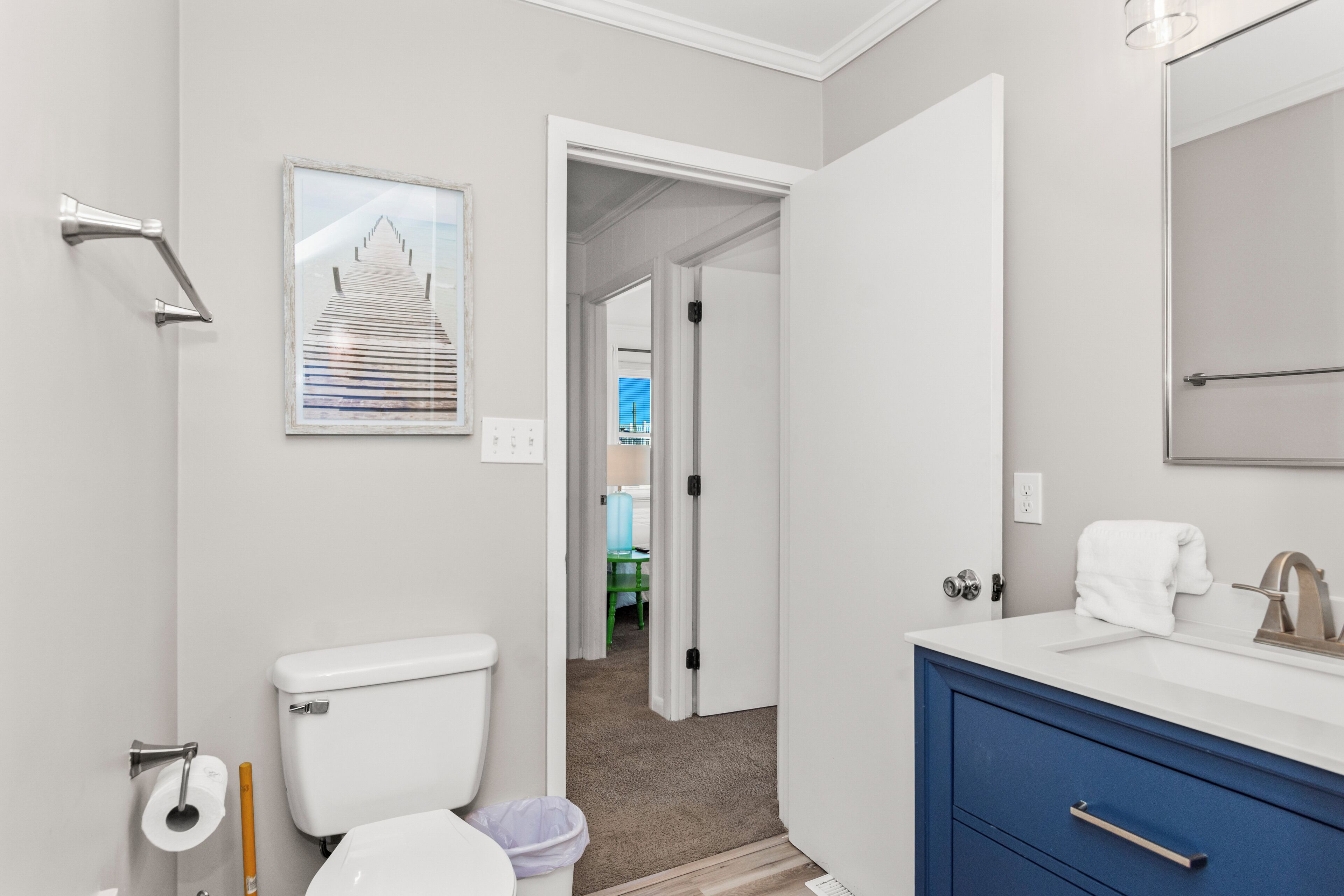 A modern bathroom with a toilet, sink, and mirror. There is a framed picture on the wall and a door leading to another room.