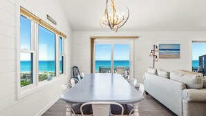 A dining area with a long table, white chairs, and a view of the ocean. - 4 BR Oceanfront Carolina Clipper East has Updated Kitchen with OF Views (Emerald Isle)