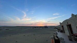 A beachside view with a stone building, a sandy beach, and a sunset in the background. - Tache By The Lake (El Faiyum)
