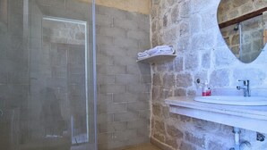 A bathroom with a glass shower enclosure, a white sink with a mirror, and a stone wall. - Tache By The Lake (El Faiyum)