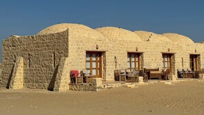 A stone building with multiple rooms, each with a door and windows. There are outdoor seating areas with chairs and tables. - Tache By The Lake (El Faiyum)
