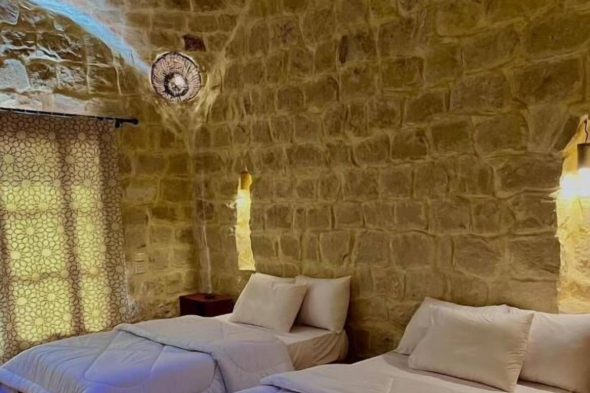Ein Zimmer mit zwei Betten, Steinwänden und einem kleinen runden Tisch.