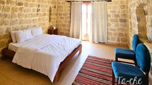 A stone-walled bedroom with a bed, a chair, and a window with curtains. - Tache By The Lake (El Faiyum)