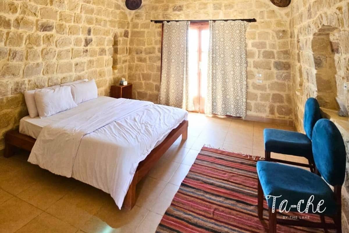 Ein Schlafzimmer mit Steinsandsteinwänden, einem Bett, einem Sessel und einem Fenster mit Vorhängen.