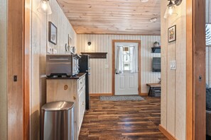 A wooden-paneled hallway with a kitchen area, a trash bin, and a door leading to another room.