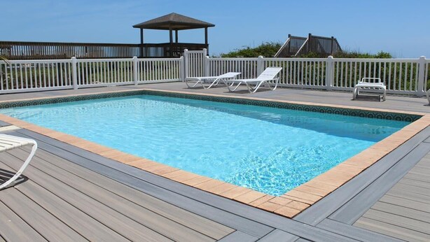 Une piscine rectangulaire dotée d’une terrasse en bois et de rampes blanches.