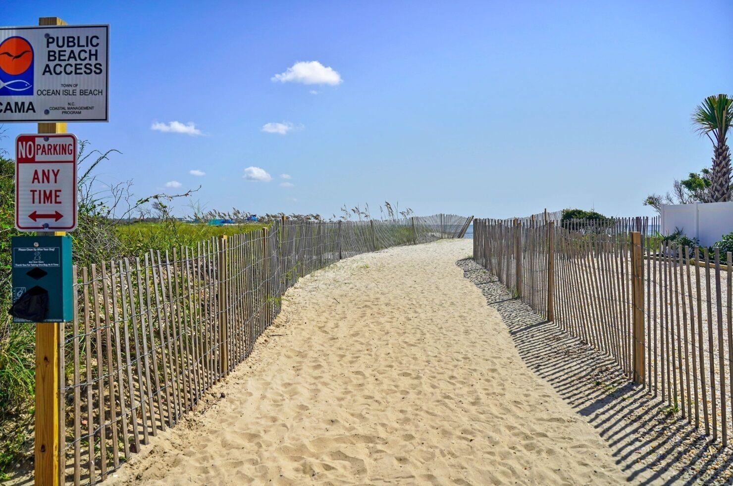 A sandy beach path with a wooden fence on both sides, a 'No Parking Any Time' sign, and a 'Public Beach Access' sign.