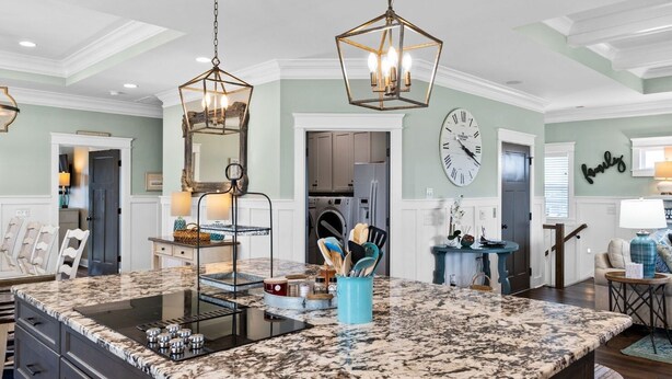A spacious kitchen with a large island, pendant lighting, and a clock on the wall. - Marshfront Home w/ Private Pool, Elevator, & Easy  Access by Williamson Realty (Ocean Isle Beach)