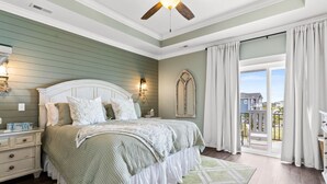 A bedroom with a large bed, a nightstand, a dresser, a ceiling fan, a window with curtains, and a view of the outside. - Marshfront Home w/ Private Pool, Elevator, & Easy  Access by Williamson Realty (Ocean Isle Beach)
