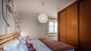 Un dormitorio con cabecera de madera, una cama grande con ropa de cama blanca y marrón, una lámpara colgante y vistas al exterior a través de una ventana.