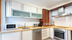 Una cocina moderna con armarios blancos, lavavajillas de acero inoxidable, horno empotrado y microondas.