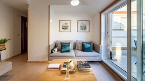 Una sala moderna con un sofá, una mesa baja con libros y un florero, y dos cuadros enmarcados con pinturas de pájaros en la pared.