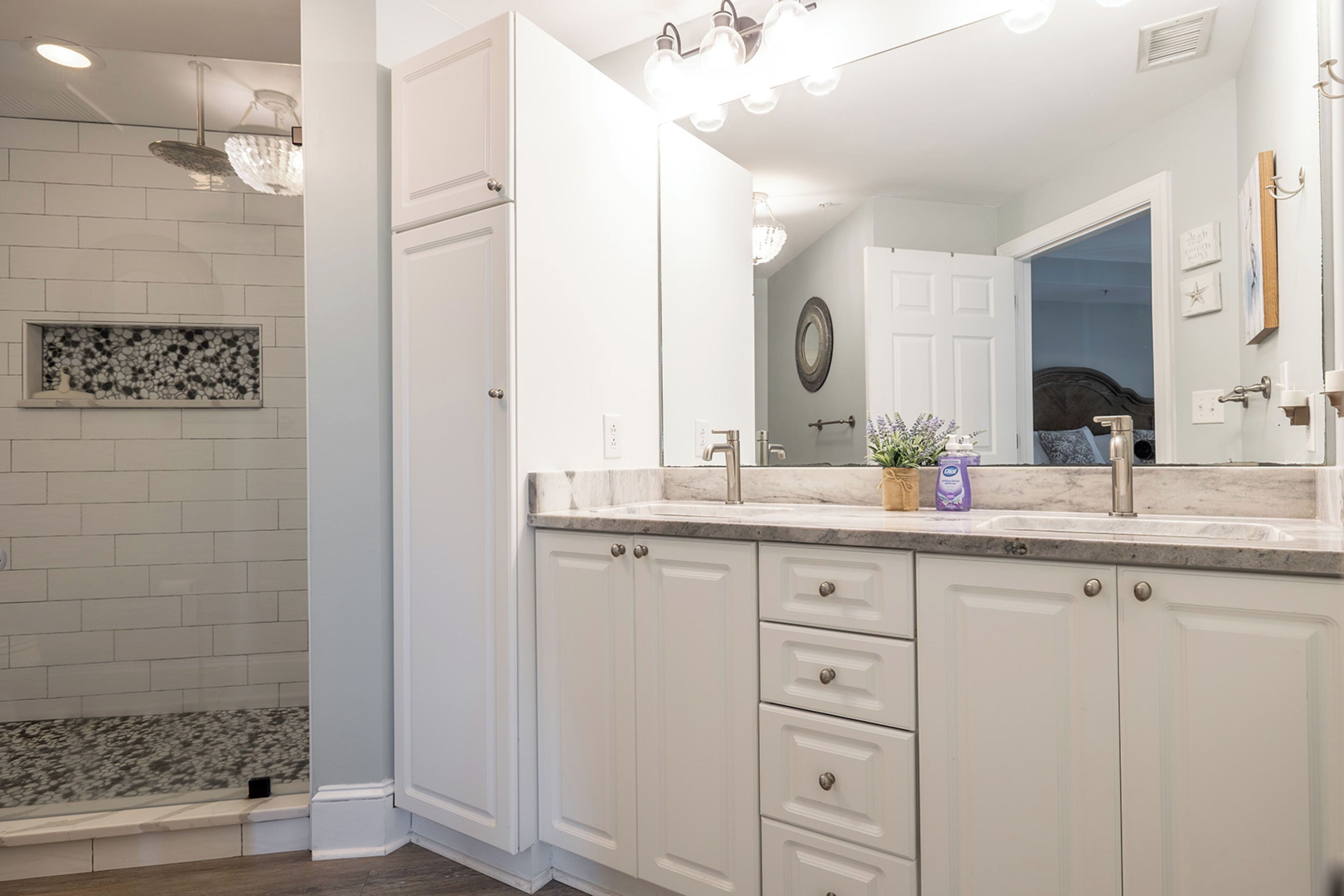 A modern bathroom with white cabinetry, a large mirror, and a shower area.