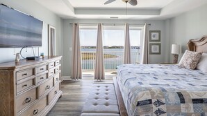Ein Schlafzimmer mit einem großen Bett, einem Deckenventilator, einer Kommode und Blick auf das Wasser.