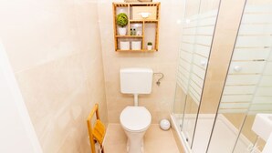 A bathroom with a toilet, a glass shower enclosure, and a wooden shelf with toiletries. - Shimmering Blue | By Radiant Apartments (Wien)