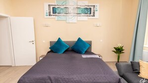 A bedroom with a bed, a grey sofa, a wall art piece, and a potted plant. - Shimmering Blue | By Radiant Apartments (Wien)