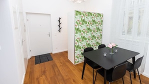 Ein Essbereich mit einem schwarzen Tisch, vier Stühlen, einer Vase mit Blumen und einer Wand mit tropischem Wandpapier.