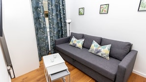 Ein modernes Wohnzimmer mit einem grauen Sofa, gemusterten Kissen, einem kleinen weißen Beistelltisch und einer Stehlampe.