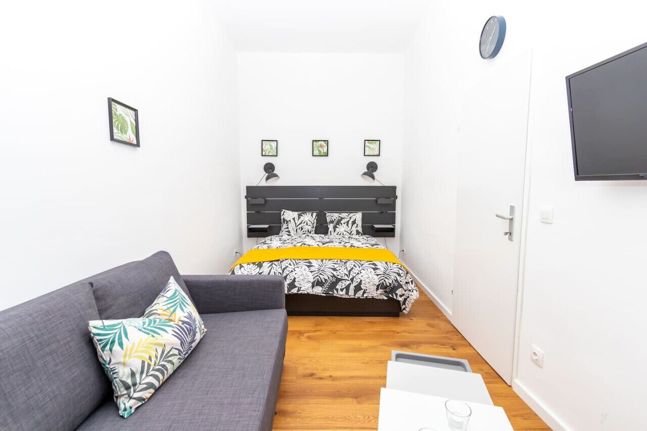 A small, modern room with a bed, a grey sofa, and a flat-screen TV.