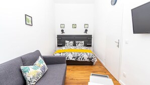Ein kleiner, moderner Raum mit einem Bett, einem grauen Sofa und einem Flachbildfernseher.