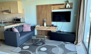A modern living space with a sofa, coffee table, TV, kitchen area, and a wooden accent wall.