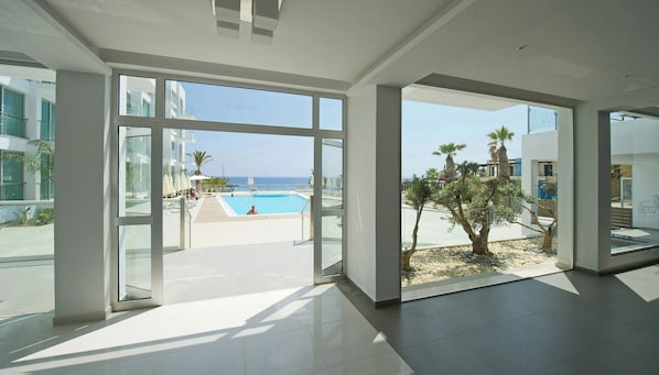Une chambre d’hôtel moderne dotée de grandes portes vitrées donnant sur un espace piscine avec vue sur l’océan.