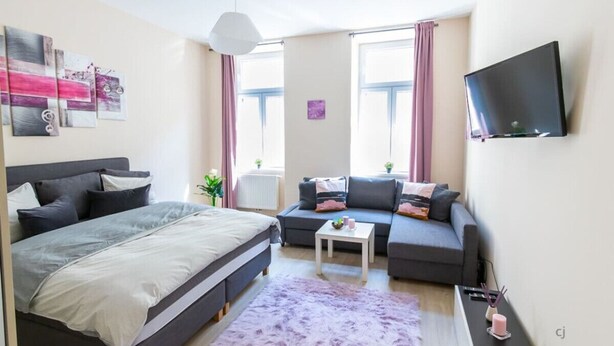 A modern bedroom with a bed, a sofa, a TV, and a window with curtains.