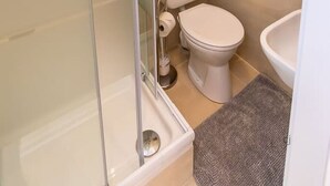 A bathroom with a glass shower enclosure, a toilet, a sink, and a towel rack.