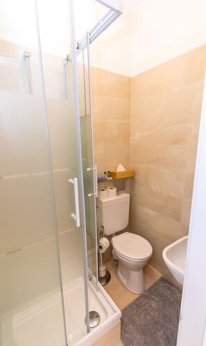 Uma casa de banho com cabine de duche em vidro, sanita, lavatório e suporte para toalhas.