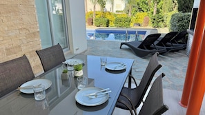 A dining area with a glass table, chairs, and a view of a swimming pool.
