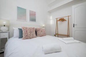 A neatly arranged bedroom with a bed, two bedside tables, a hanging wooden rack, and two wall-mounted lamps. - Beautiful Mews Cottage | 6 min walk to Rottingdean Beach | Near Brighton (Rottingdean)