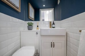 A bathroom with white tiles, a sink, a toilet, and a mirror. - Beautiful Mews Cottage | 6 min walk to Rottingdean Beach | Near Brighton (Rottingdean)