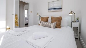 A neatly made bed with white linens and two pillows, a bedside table with a lamp, and a painting on the wall. - Beautiful Mews Cottage | 6 min walk to Rottingdean Beach | Near Brighton (Rottingdean)