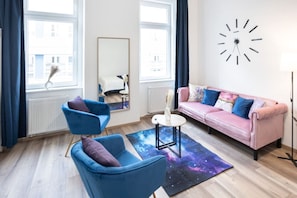 Uma sala de estar moderna com um sofá rosa, poltronas azuis, uma mesa de centro redonda e um tapete com tema espacial.