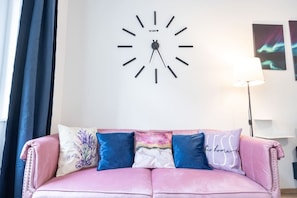 Um sofá rosa com almofadas decorativas e um relógio de parede em cima.