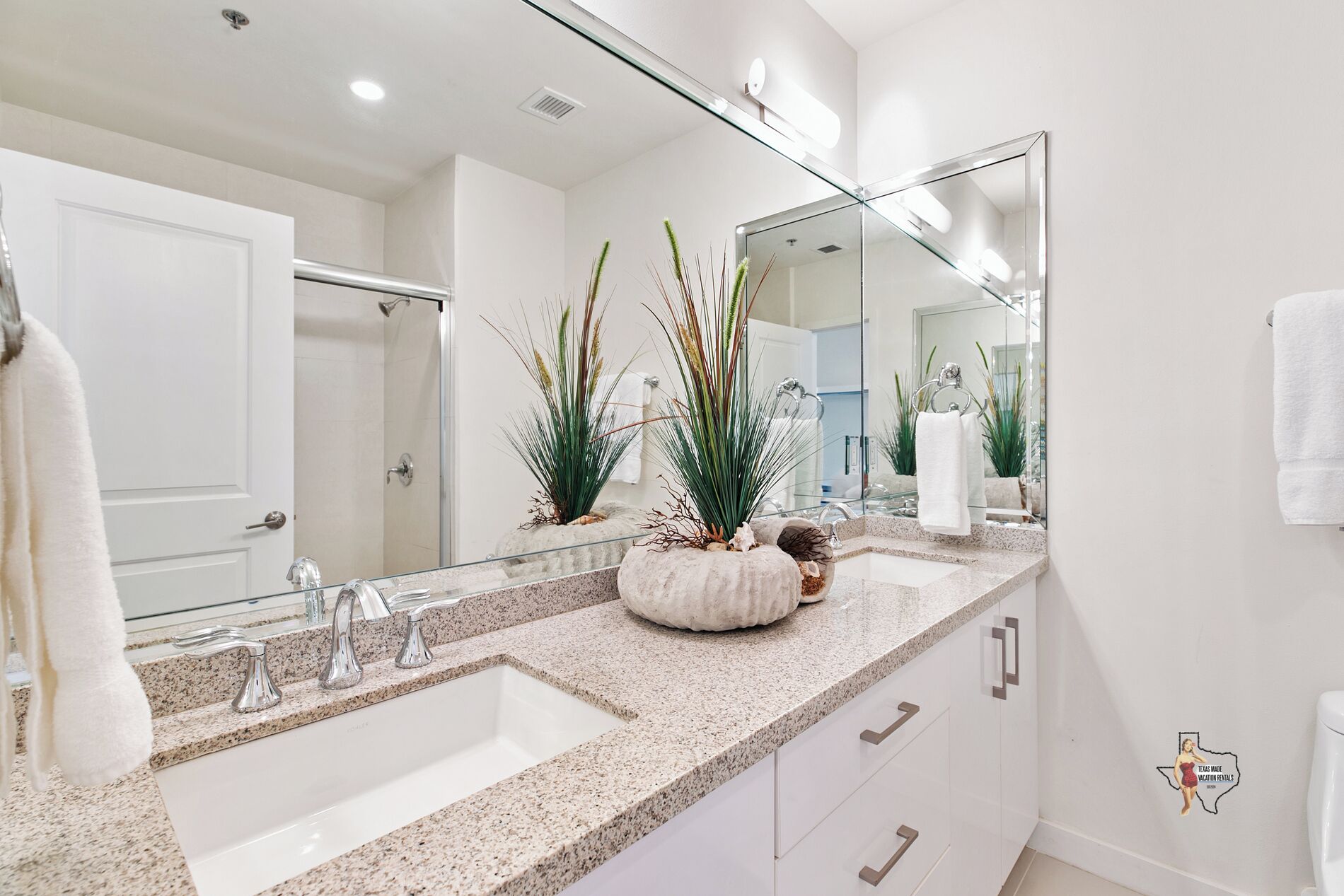 A modern bathroom with a large mirror, two sinks, and a decorative plant centerpiece.