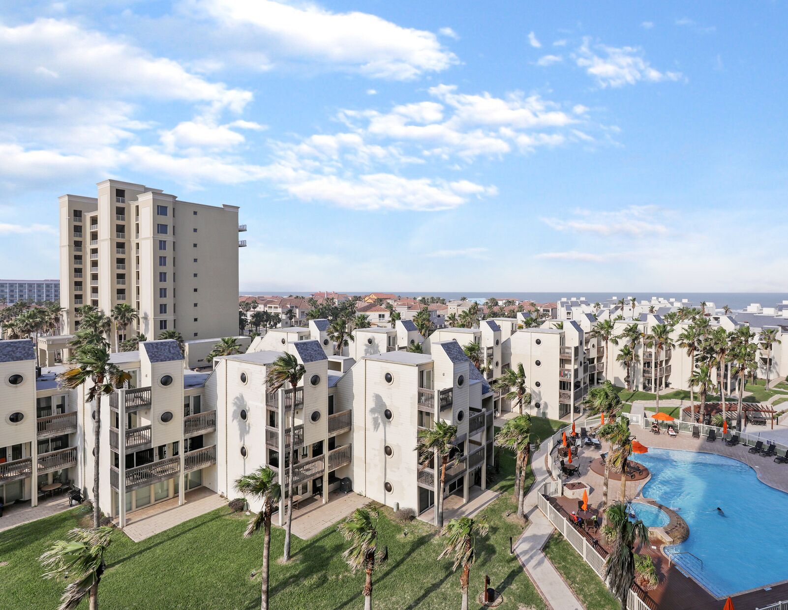 A resort with multiple-story buildings, a swimming pool, and palm trees.