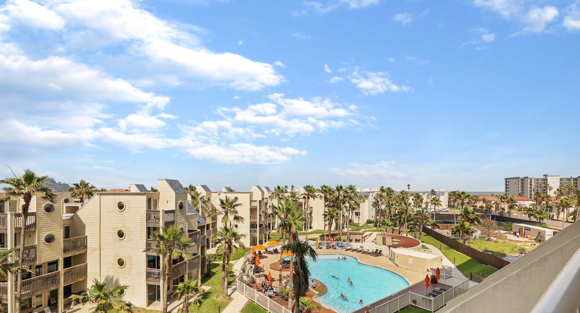 A resort with multiple-story buildings, a central swimming pool, and palm trees.