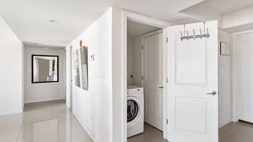 Un pasillo moderno y amplio con lavadora, una puerta con perchero y un espejo que refleja la habitación.