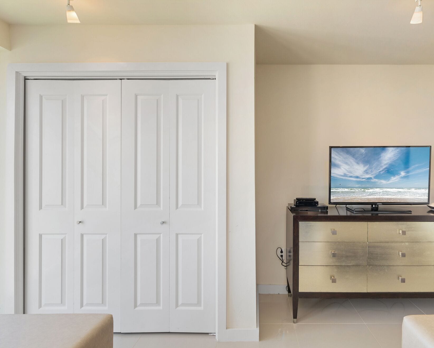 A room with a closed white door, a television on a wooden cabinet, and a tiled floor.