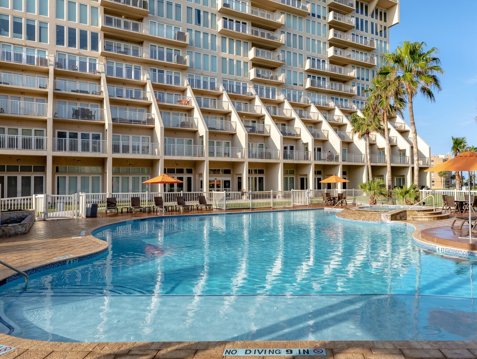 A hotel with a large swimming pool, multiple balconies, and palm trees.