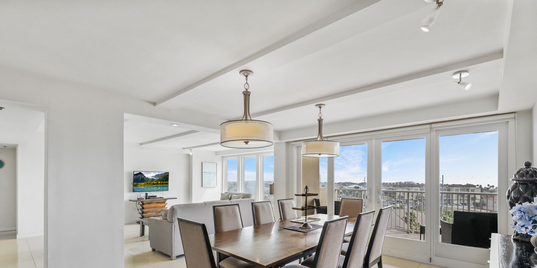 A spacious dining area with a large table and chairs, a chandelier, and a view of the city through large windows.