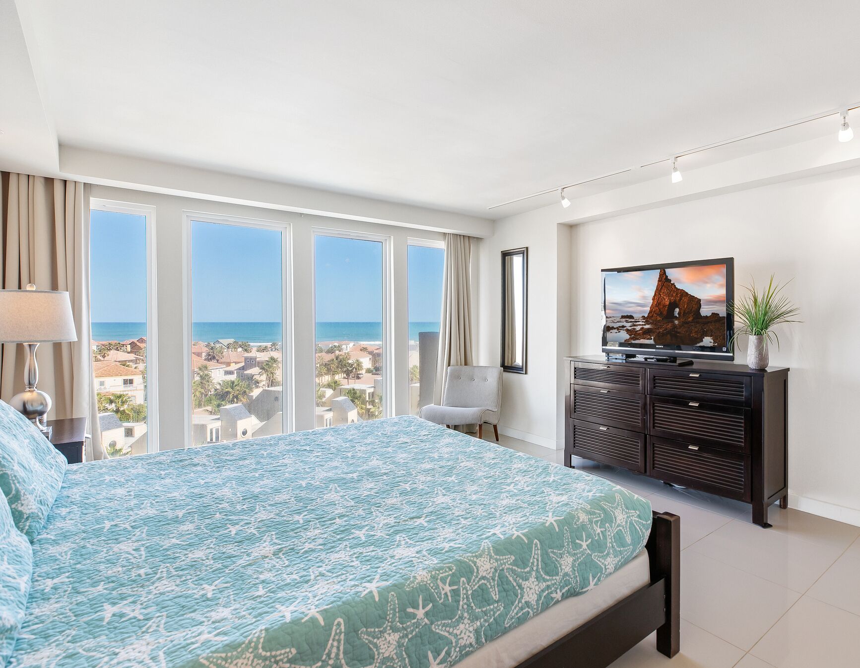 Ein Schlafzimmer mit Bett, Fernseher, Kommode und Meerblick.