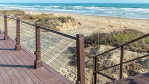 Une promenade en bois mène à une plage de sable, avec l’océan et ses vagues en arrière-plan.